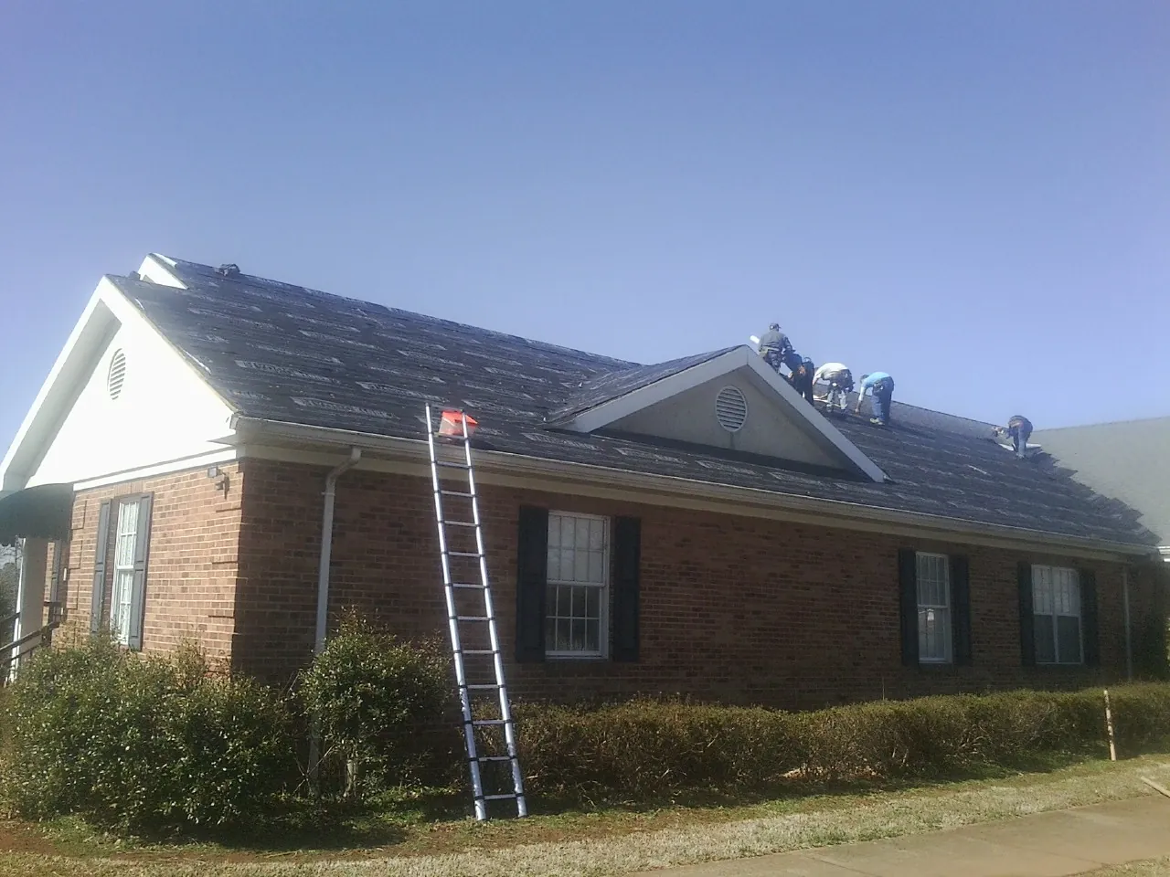 Crew tearing shingles off a brick ranch roof with a ladder set — Metal Roof Repair work by our crew in Crossville